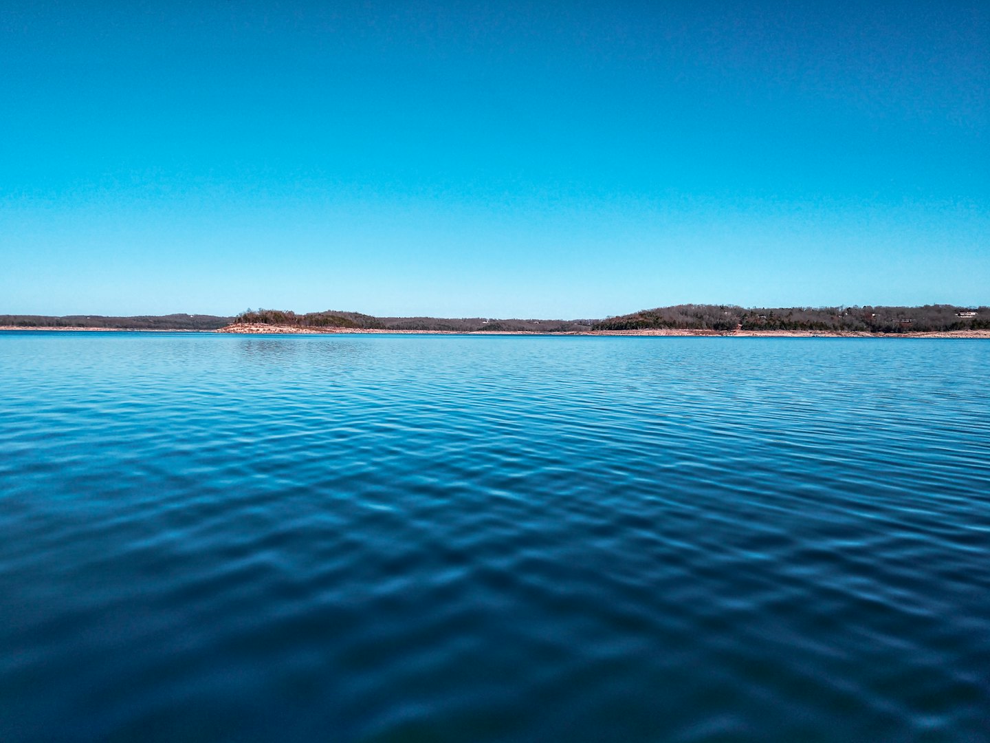 Mjuka krusningar rör sig över en lugn sjö under skogsklädda kullar.